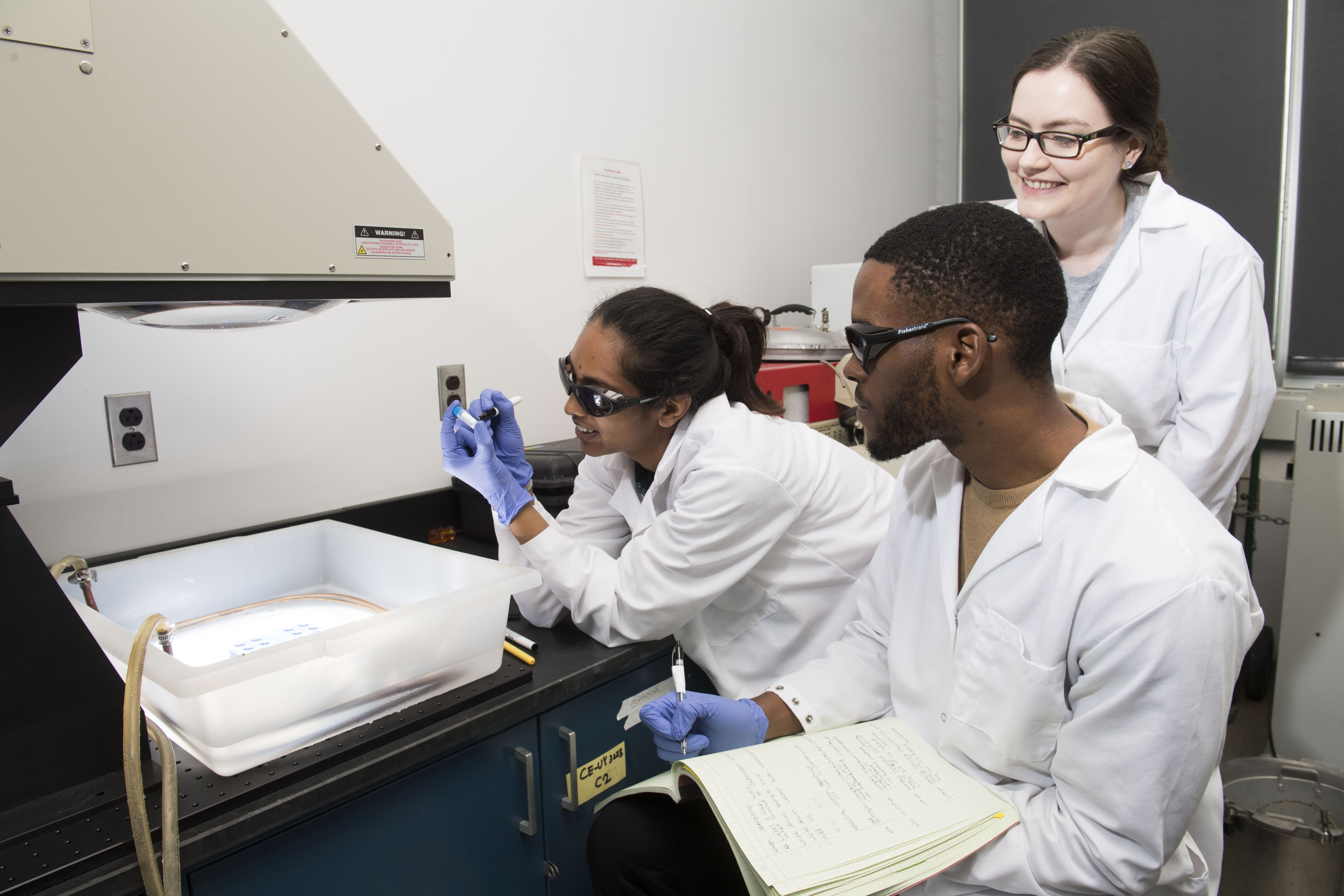 Group of three students in lab coats, working in a lab